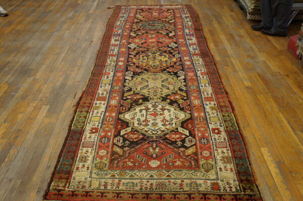 Geometric runner rug in red, black, and cream on worn light brown wood floors.