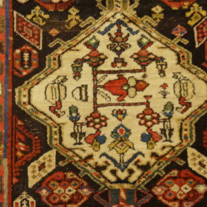 Traditional rug close-up showing a cream medallion, red border, and multicolored geometric patterns on black.