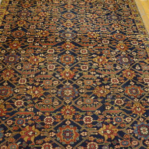 Navy rug with an all-over geometric and floral pattern in red, gold, and blue on wood flooring.