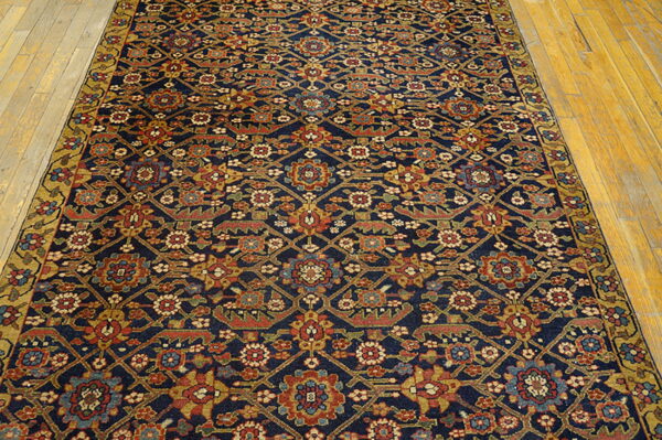 Navy rug with an all-over geometric and floral pattern in red, gold, and blue on wood flooring.