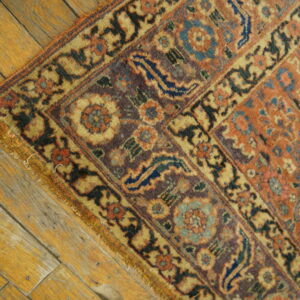 Ornate rust, purple, and yellow floral rug corner rests diagonally across wide, distressed wood planks.