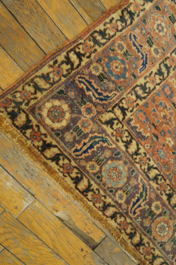 Ornate rust, purple, and yellow floral rug corner rests diagonally across wide, distressed wood planks.