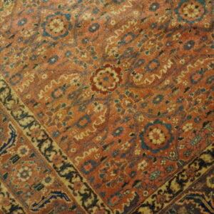 A low-pile rug with intricate orange, blue, and gold floral patterns rests on wooden plank flooring.