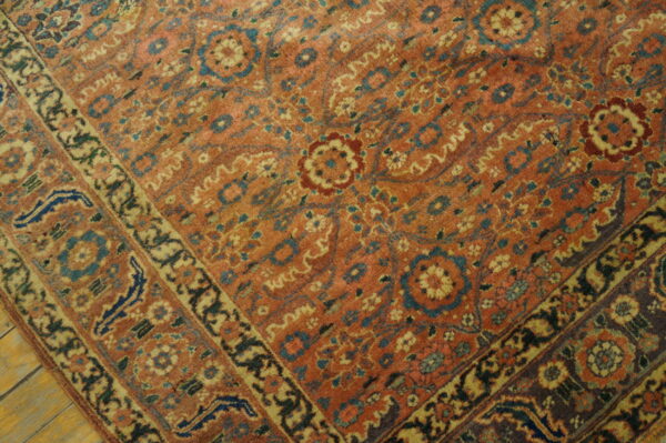 A low-pile rug with intricate orange, blue, and gold floral patterns rests on wooden plank flooring.
