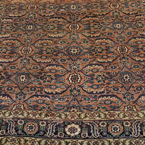 Rust and blue traditional medallion rug with floral and vine patterns lies on rustic wooden floorboards.