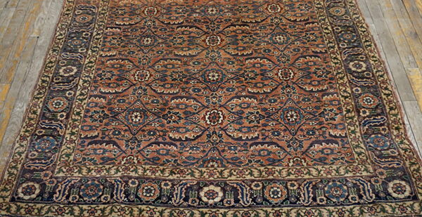 Rust and blue traditional medallion rug with floral and vine patterns lies on rustic wooden floorboards.