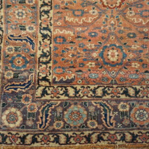 Muted coral, blue, and purple floral rug corner rests on light wood planks.