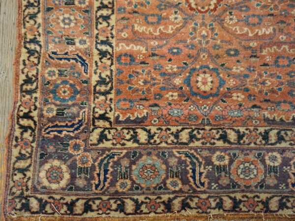 Muted coral, blue, and purple floral rug corner rests on light wood planks.