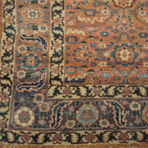 Close-up of an intricate rug corner featuring rust and blue colors next to rustic gray wood floorboards.