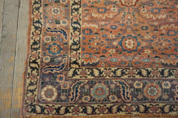 Close-up of an intricate rug corner featuring rust and blue colors next to rustic gray wood floorboards.