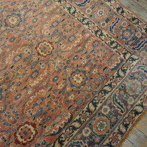 Dusty rose floral rug featuring ornate borders in navy and purple rests on distressed wooden floors.