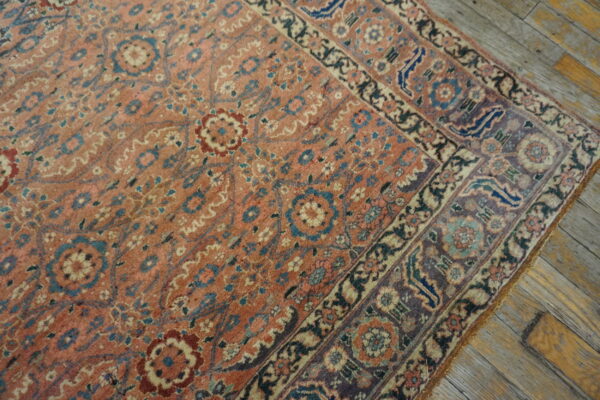 Dusty rose floral rug featuring ornate borders in navy and purple rests on distressed wooden floors.