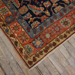 Traditional rug corner featuring navy, red, gold, and light blue patterns on distressed wood flooring.