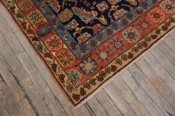 Traditional rug corner featuring navy, red, gold, and light blue patterns on distressed wood flooring.