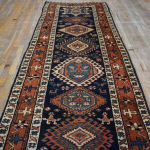 Geometric navy and rust runner rug with cream accents lying on rustic gray wood floors.