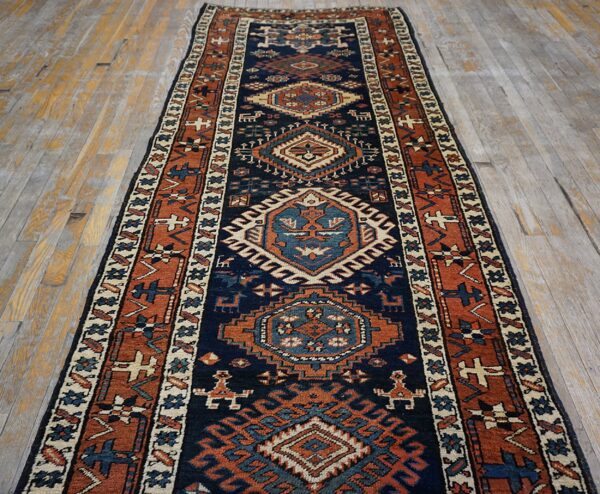 Geometric navy and rust runner rug with cream accents lying on rustic gray wood floors.