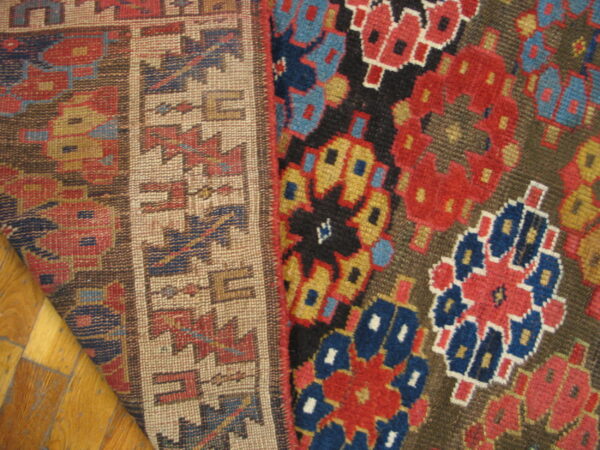 Geometric red, blue, and gold pile rug detail beside a tan patterned flatweave border on wood floor.