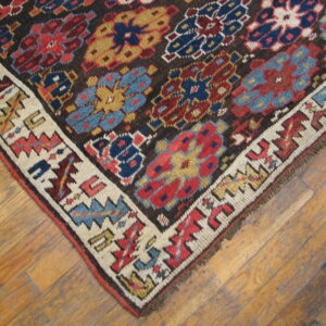 Colorful, low-pile rug displaying geometric patterns on a dark field and white border, placed on wooden flooring.