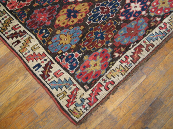 Colorful, low-pile rug displaying geometric patterns on a dark field and white border, placed on wooden flooring.