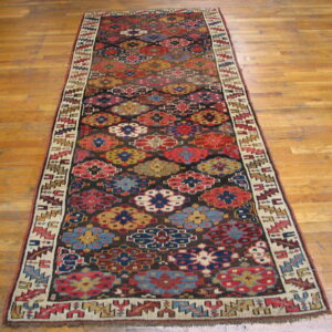 A long runner rug featuring colorful geometric floral motifs on a dark ground, lying on hardwood flooring.