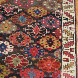 Geometric floral rug in red, black, blue, and gold resting on light brown wood plank flooring.