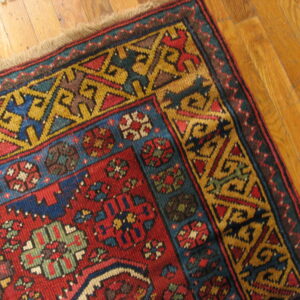 A geometric rug in red, blue, and gold with complex borders rests on honey-toned wood flooring.