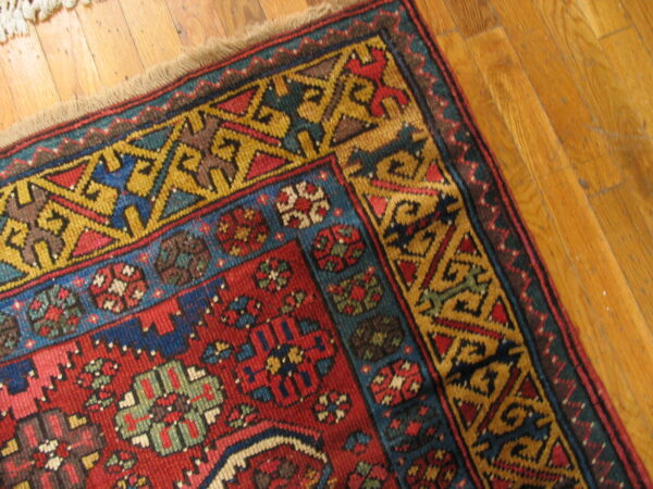 A geometric rug in red, blue, and gold with complex borders rests on honey-toned wood flooring.