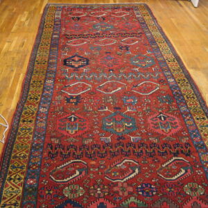 Red geometric runner rug featuring tribal motifs in blue, yellow, and black on plank wood flooring.