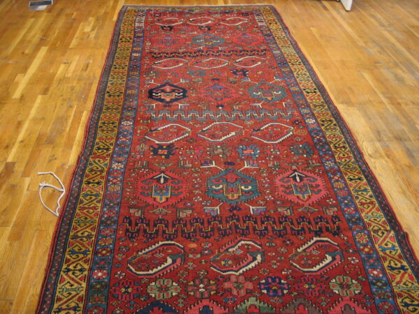 Red geometric runner rug featuring tribal motifs in blue, yellow, and black on plank wood flooring.
