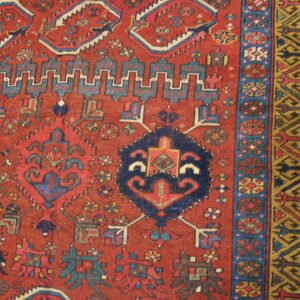 Close-up of a rust-red rug showing geometric blue medallions and multi-layered gold and brown borders.