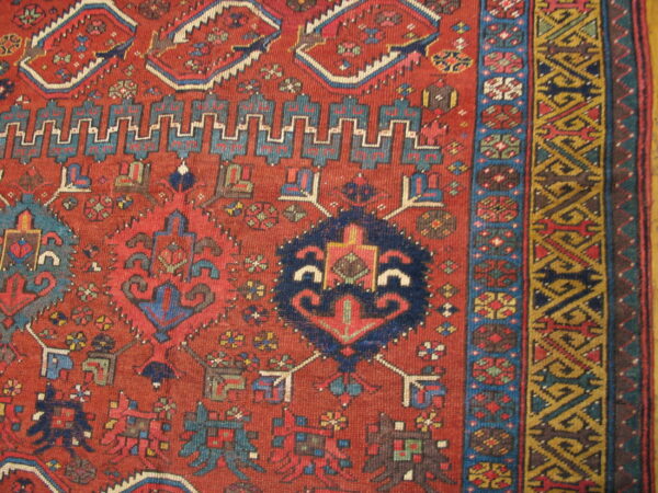 Close-up of a rust-red rug showing geometric blue medallions and multi-layered gold and brown borders.