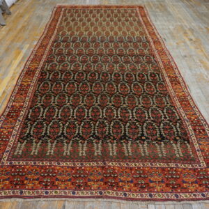 Dark floral repeating patterns fill this long red-bordered runner displayed on faded wood flooring.