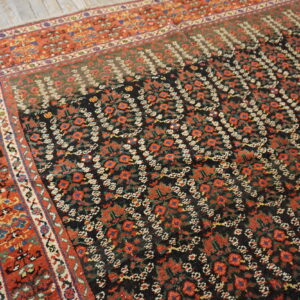 Black rug with repeating red floral motifs and a wide rust-colored geometric border on wood floors.