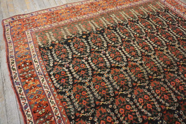 Black rug with repeating red floral motifs and a wide rust-colored geometric border on wood floors.