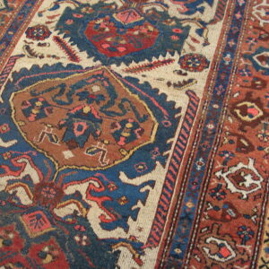 Low pile rug featuring stylized geometric patterns in blue, terracotta, and ivory laid over wood flooring.