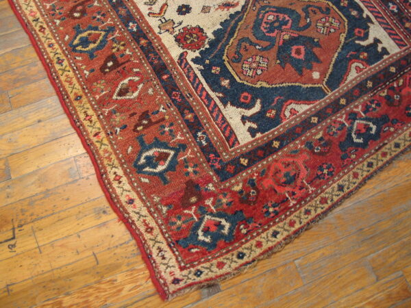 Corner of a traditional rug with rust, navy, and beige patterns on worn, light brown wood planks.