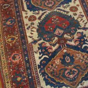 Geometric patterned rug in deep reds, navy, and cream rests on horizontal light brown wood floor.
