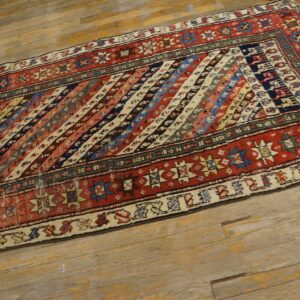 Multi-colored runner rug with diagonal stripes and red geometric borders on rustic wood flooring.