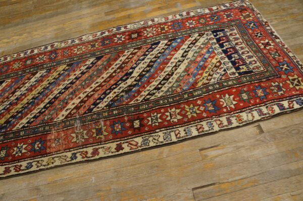 Multi-colored runner rug with diagonal stripes and red geometric borders on rustic wood flooring.