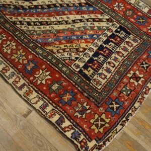 Low-pile geometric rug with striped center and red borders rests on distressed light wood flooring.
