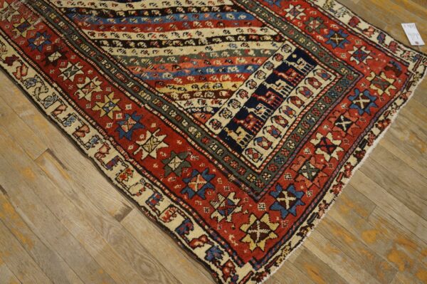 Low-pile geometric rug with striped center and red borders rests on distressed light wood flooring.