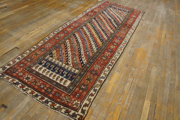 Multicolored geometric runner rug with a rust-red border lying diagonally on distressed wide plank wood.