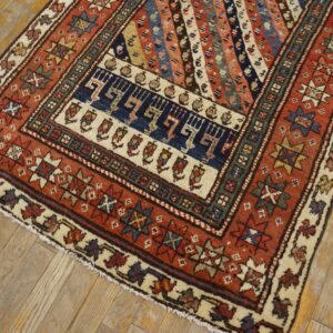Rust and blue geometric rug featuring diagonal stripes and medallions, displayed on light wooden plank flooring.