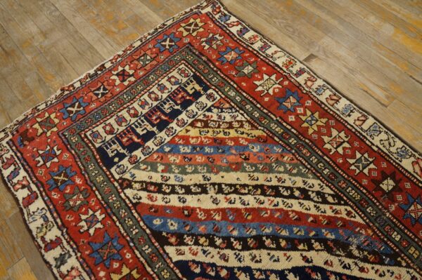 Red, blue, and cream geometric rug with horizontal stripes rests on light, distressed wood floorboards.