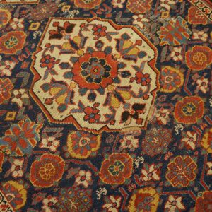 Highly detailed view of a navy, red, and gold patterned rug centered by an octagonal cream medallion.