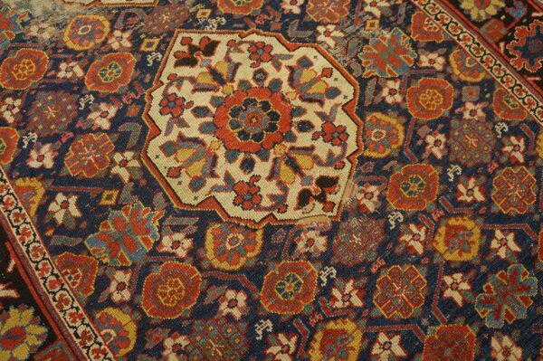 Highly detailed view of a navy, red, and gold patterned rug centered by an octagonal cream medallion.