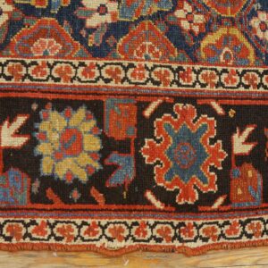 The detailed border of a dark blue, red, and cream patterned rug lying on light hardwood flooring.