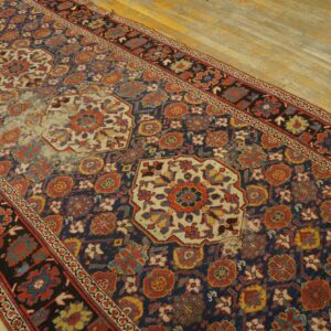 A distressed runner rug with navy, red, and cream medallions lies on light colored wood floors.