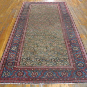 Traditional runner rug with an all-over pattern in muted green and tan, framed by red and blue borders on wood floors.
