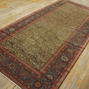 Traditional low-pile rug with a muted olive field and contrasting red and blue patterned borders on worn wood planks.